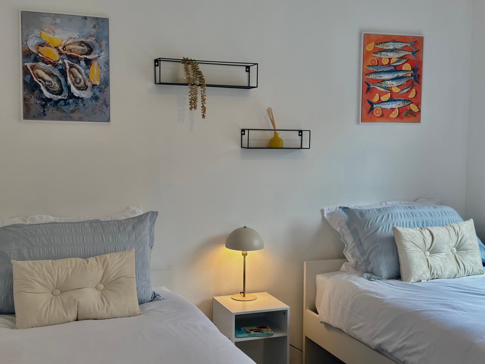 The Barrows — twin bedroom with lamplight and seaside artwork